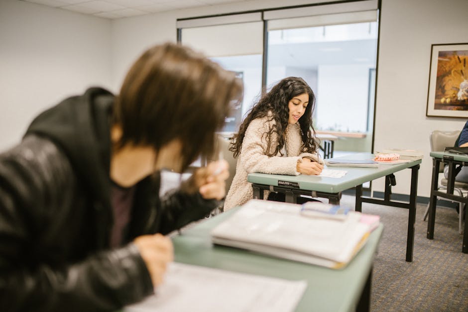 Two students focused on an exam in a classroom setting during daylight