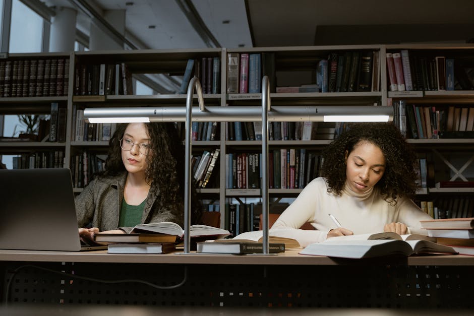 Two female students studying with books and laptops in a modern library setting